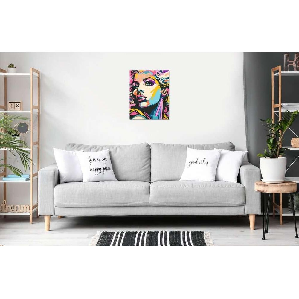 Ein graues Sofa mit Kissen und Pop-Art-Frauenbild an der weißen Wand, eingerahmt von Regalen und Pflanzen.