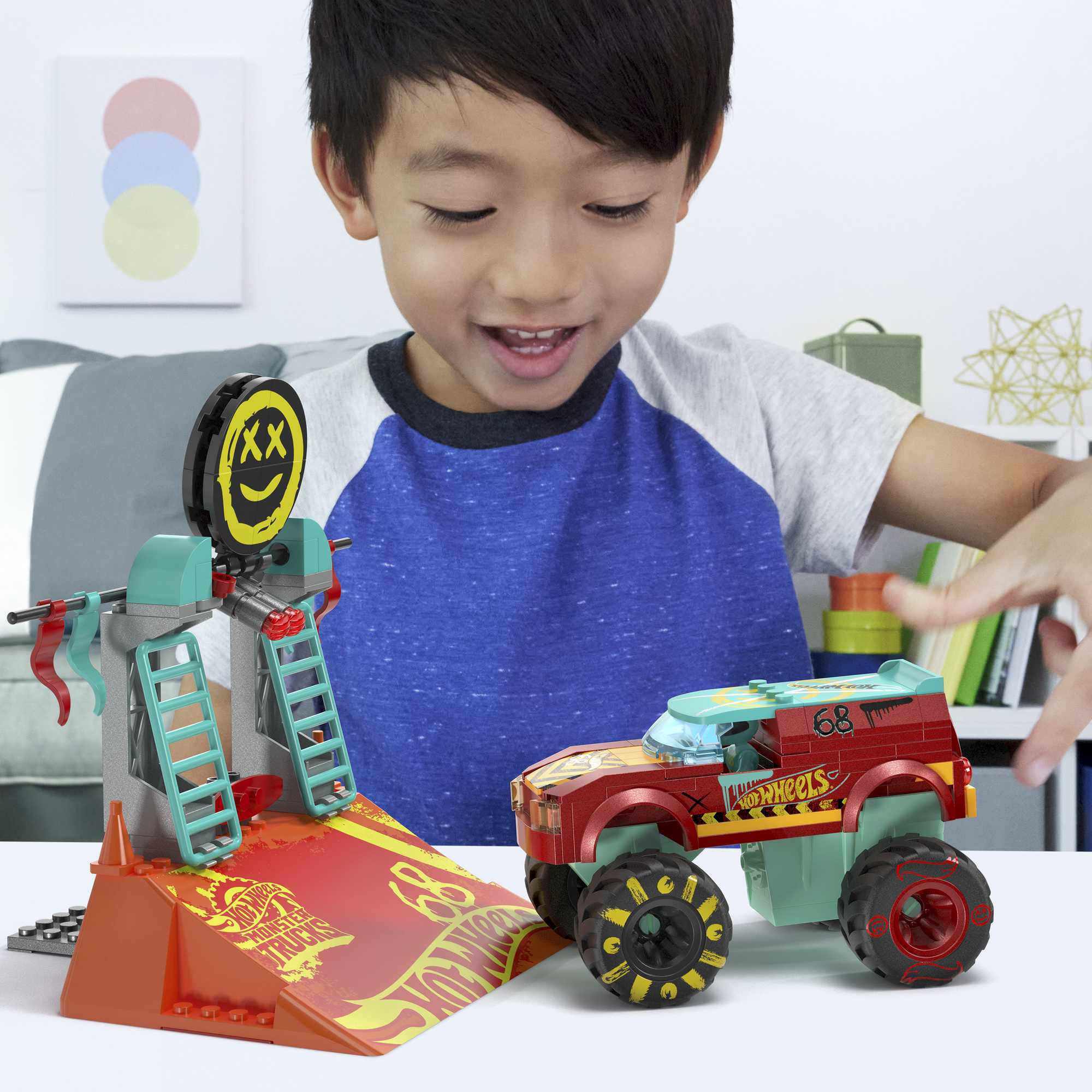 Ein Junge lächelt, während er mit einem roten Spielzeug-Monster-Truck und einer Rampe spielt.