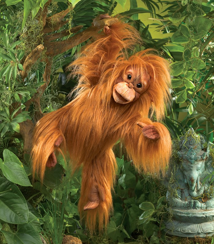 Un orang-outan en peluche est suspendu à une branche dans la jungle devant une statue d'éléphant en pierre.