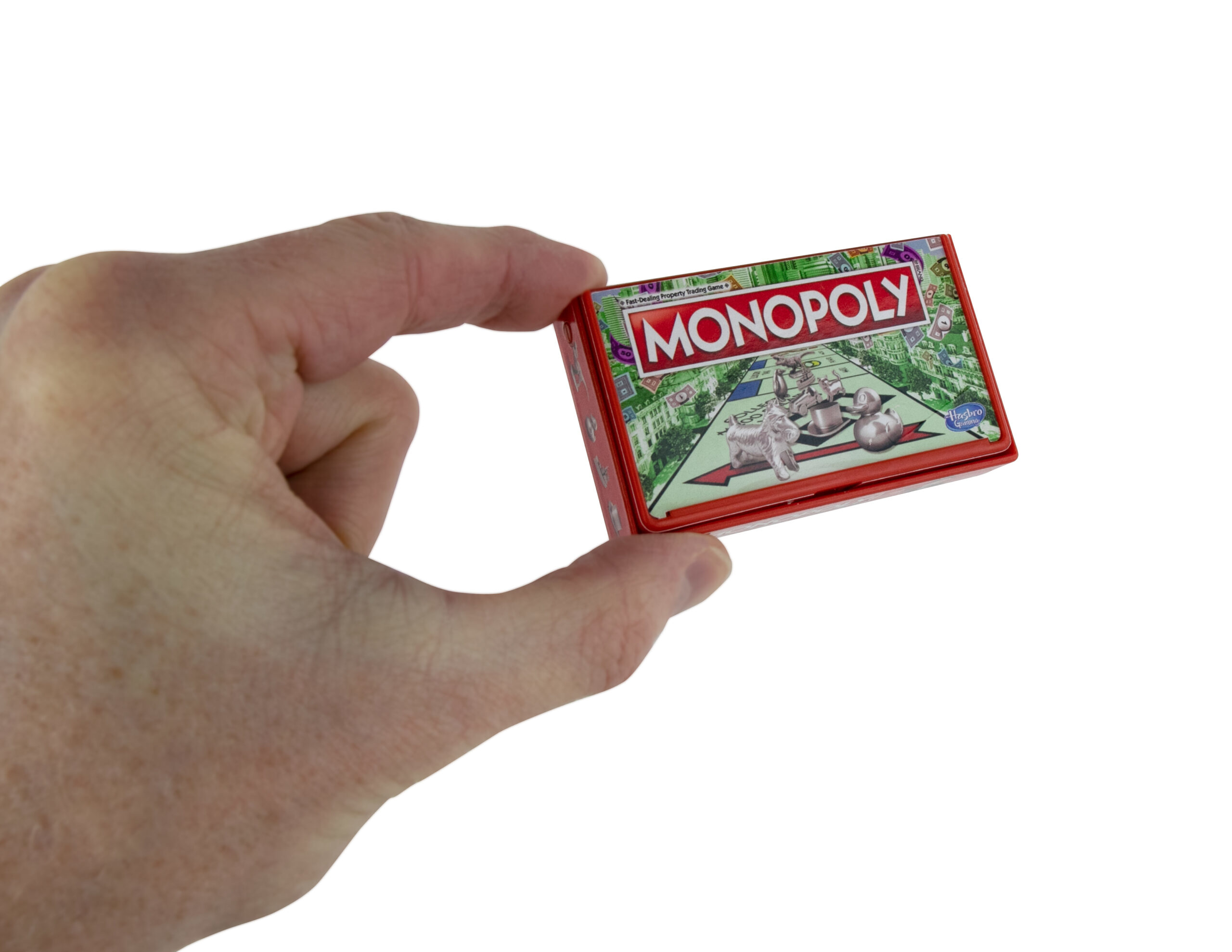 Eine Hand hält ein Miniatur-Monopoly-Brettspiel in einer roten Blechdose vor weißem Hintergrund.