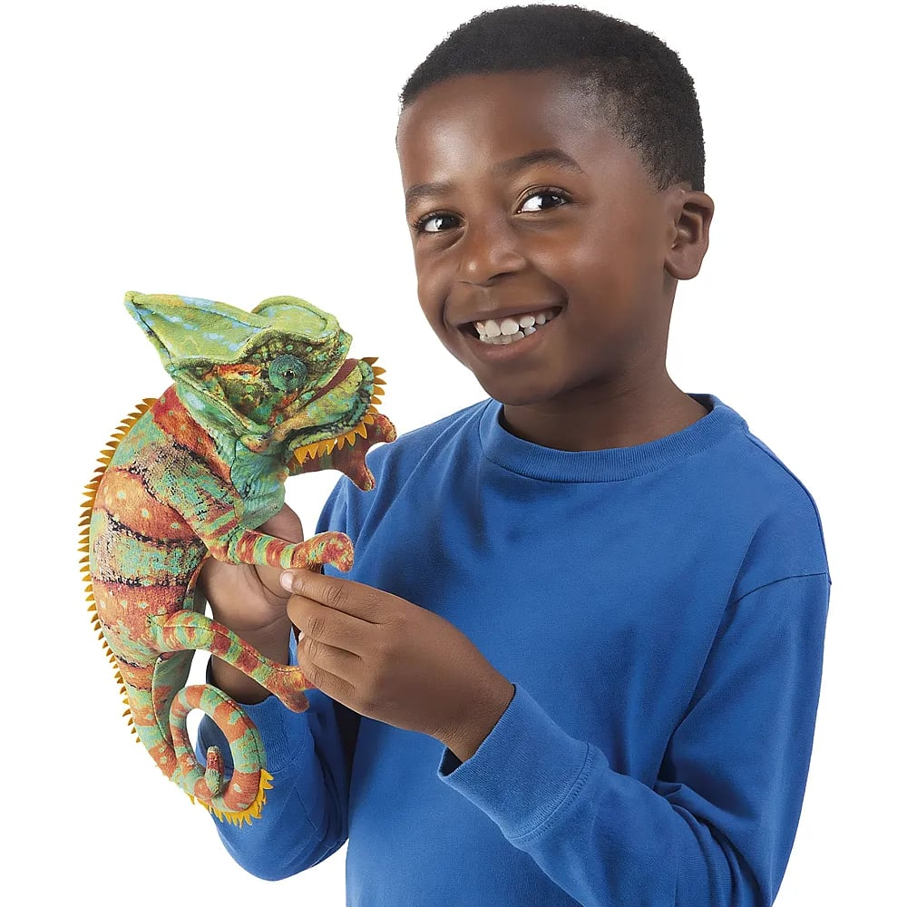 Ein lächelnder Junge in einem blauen Pullover hält eine große Plüsch-Chamäleonpuppe.