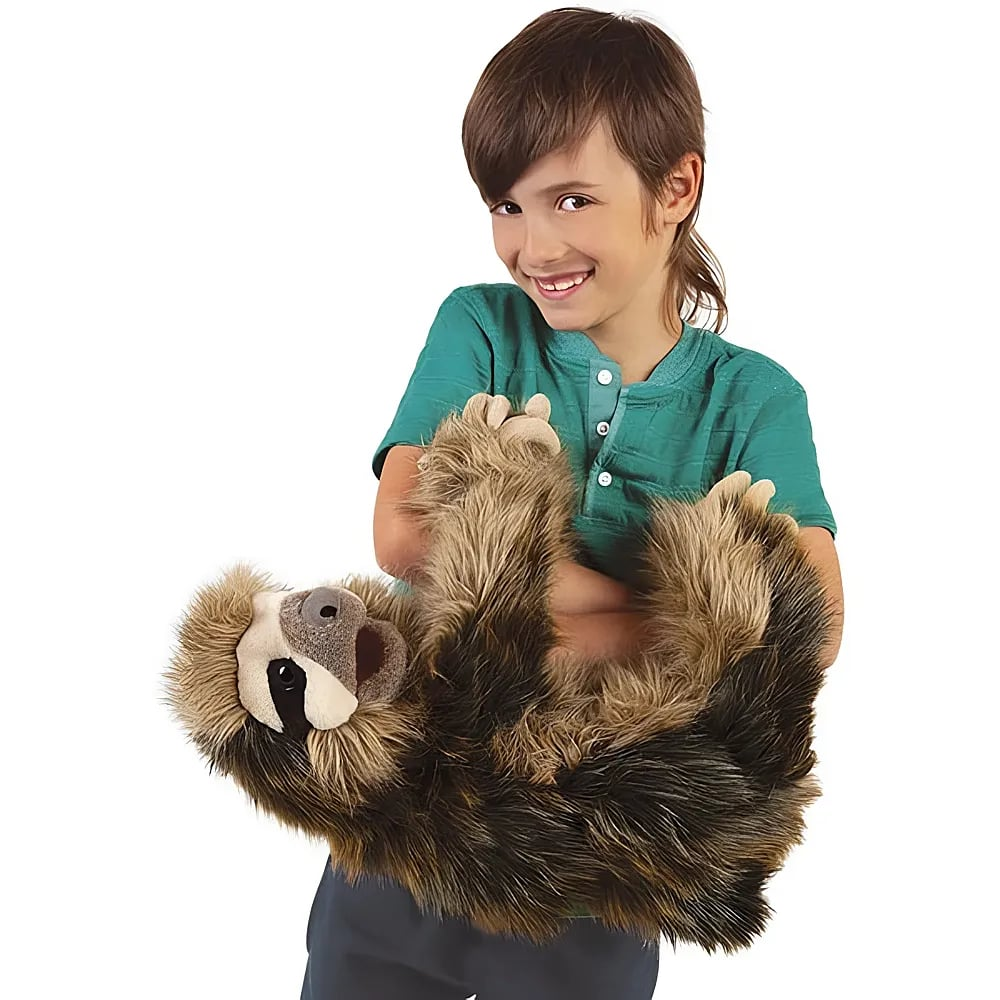 Un bambino sorridente tiene un grande burattino di peluche a forma di bradipo su sfondo bianco.