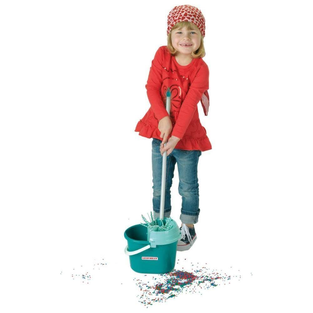 Una bambina con maglietta rossa e bandana usa un secchio verde e un mocio per pulire particelle colorate dal pavimento.