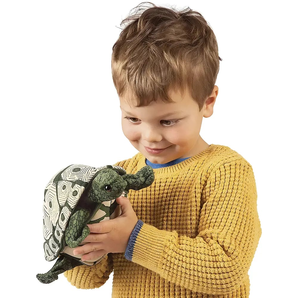 Ein junger Junge im gelben Pullover hält lächelnd eine Plüsch-Meeresschildkröte.
