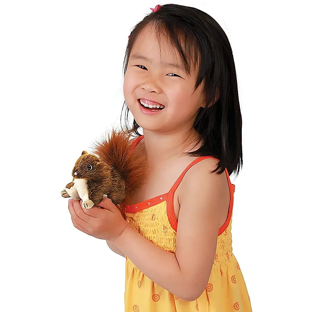 Ein smiling kleines Mädchen im gelben Kleid hält eine Plüsch-Eichhörnchenpuppe.
