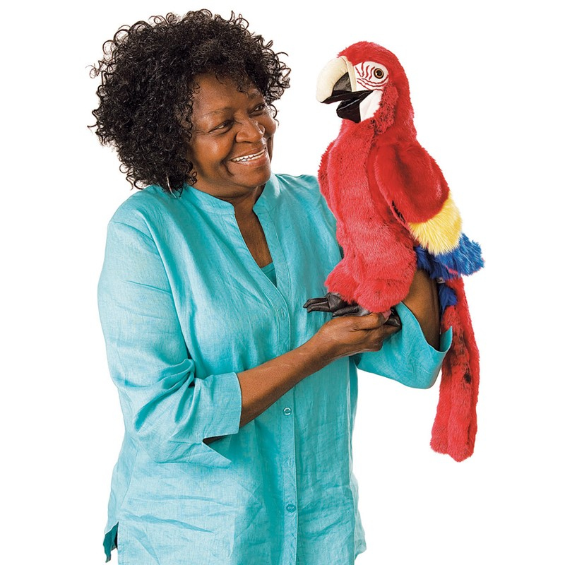 Eine Frau in blauem Hemd hält eine große, rote Papageienpuppe und lächelt.