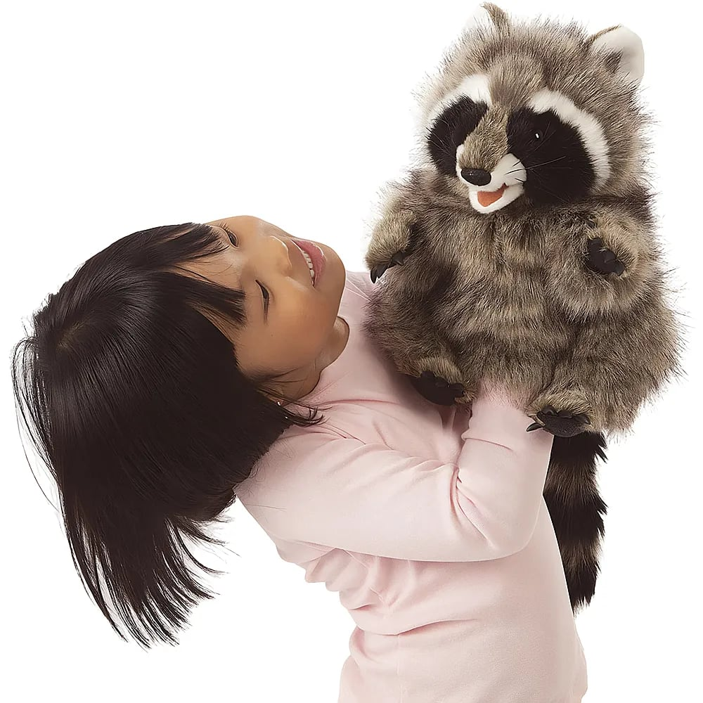 Ein junges Mädchen in einem rosa Pullover hält eine große Waschbär-Handpuppe und lächelt.