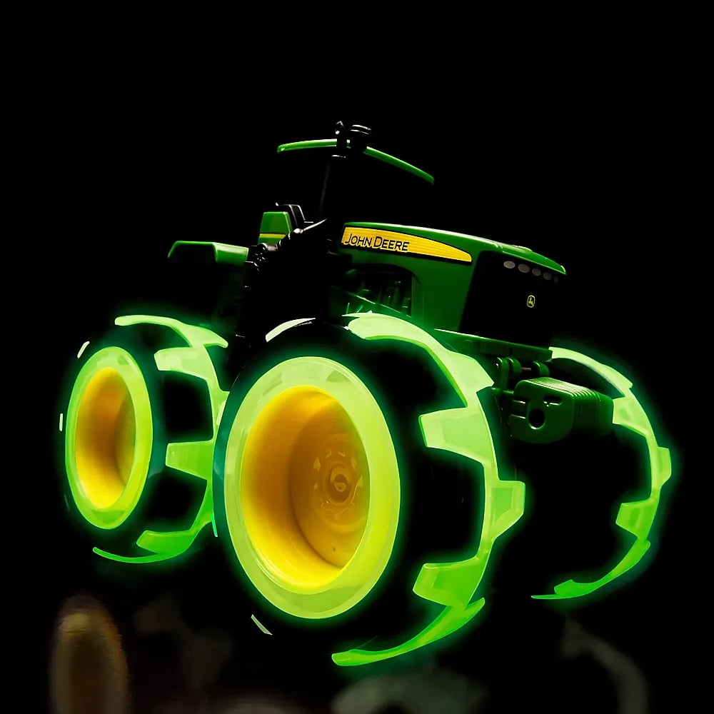 Ein John-Deere-Spielzeugtraktor mit leuchtend grünen und gelben Rädern vor schwarzem Hintergrund.
