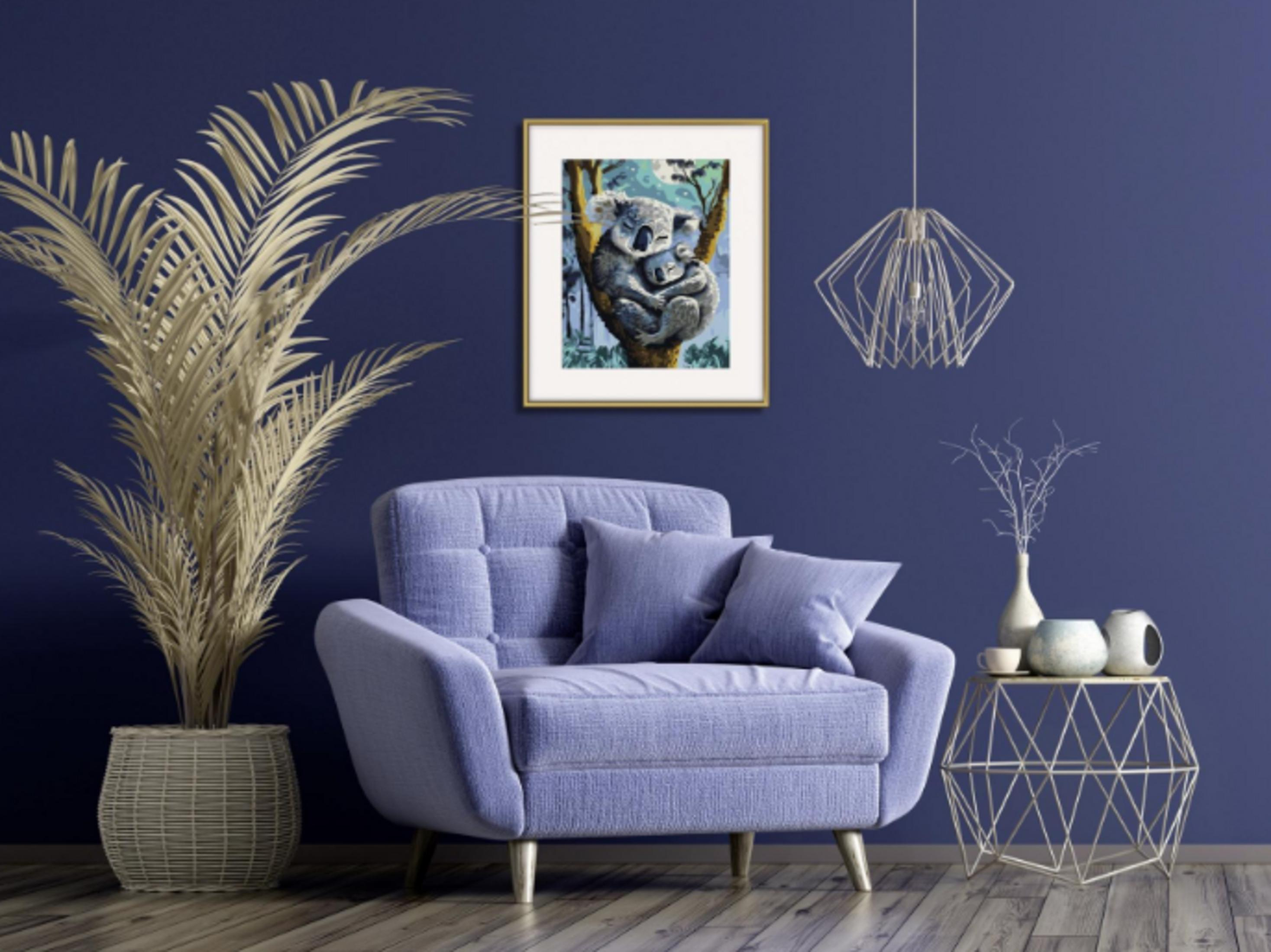 Ein lilafarbener Sessel vor einer blauen Wand, links eine große Pflanze, rechts ein kleiner Tisch mit Deko und darüber eine Lampe.