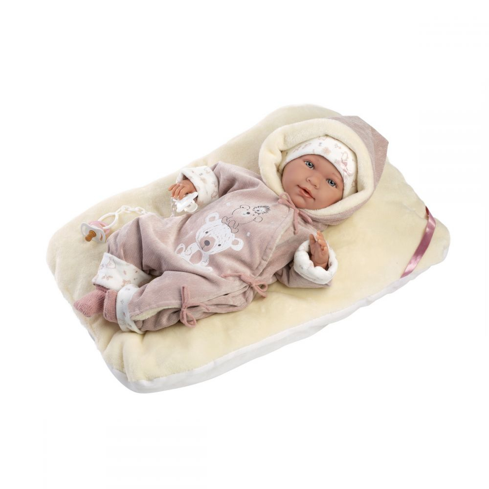 Eine Babypuppe in rosafarbenem Strampler liegt auf einem hellen Kissen neben einem Schnuller.