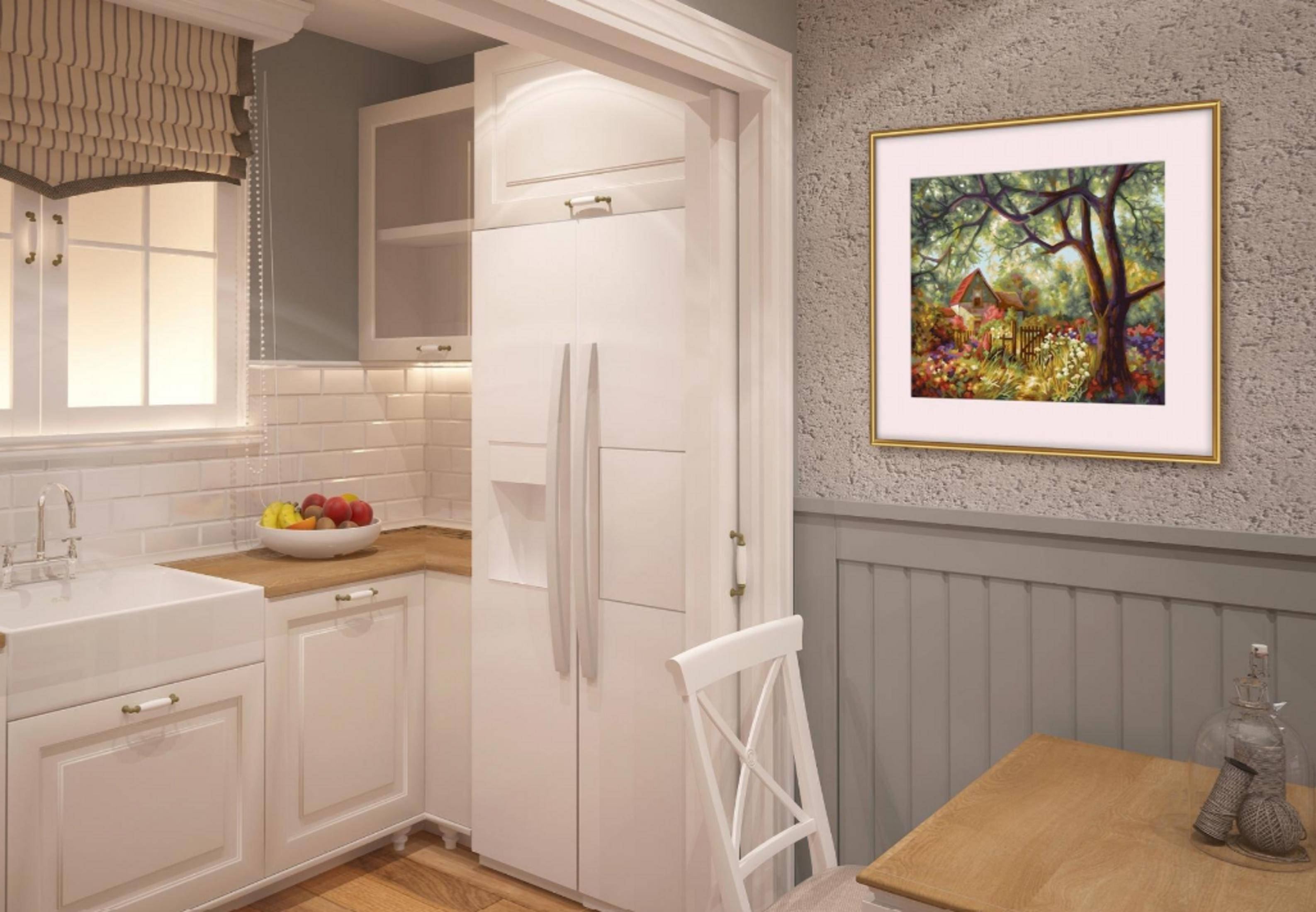 Eine helle Küche mit weißem Kühlschrank, weißem Schrank, Obstschale und einem gerahmten Gemälde an der Wand.