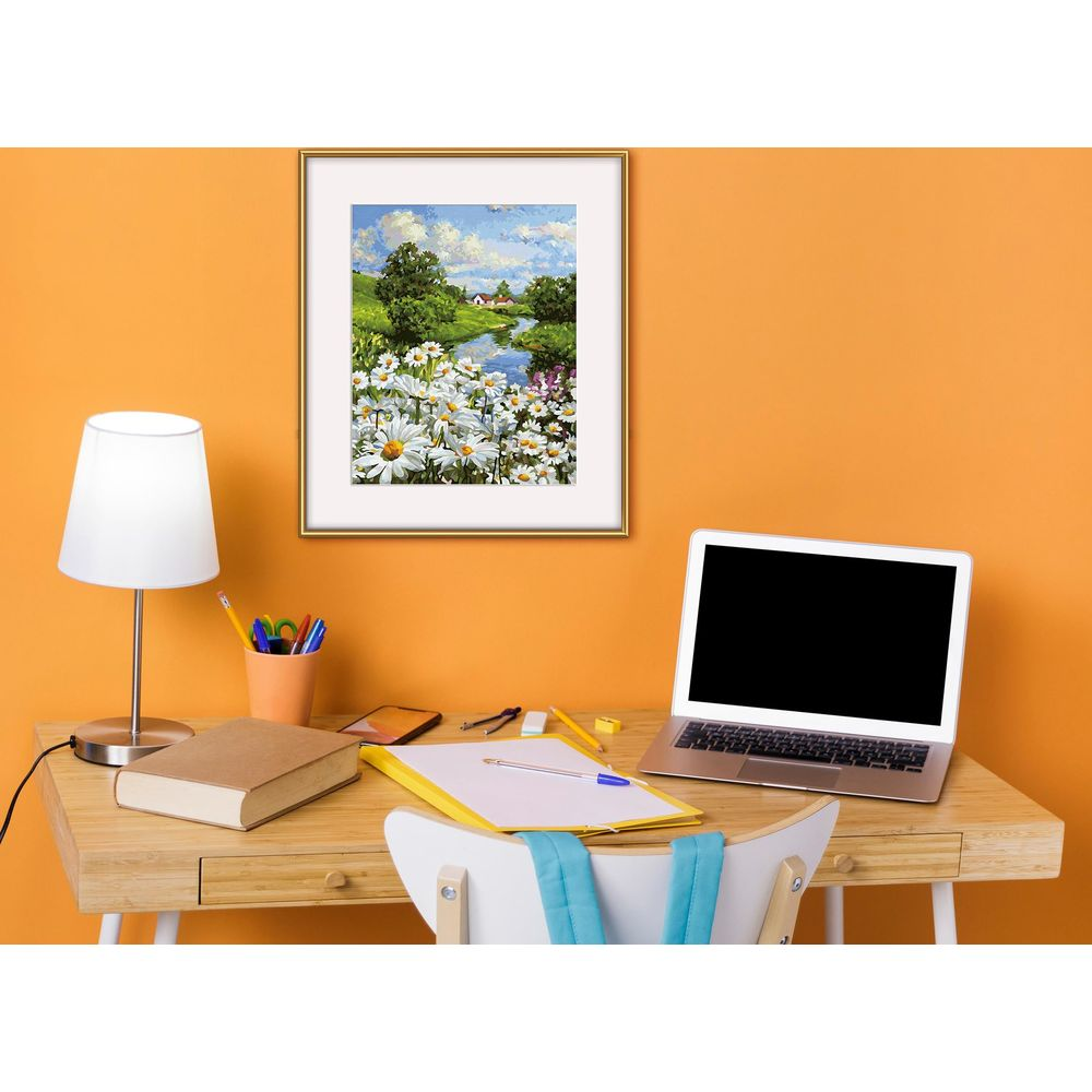 Ein Schreibtisch mit Laptop, Lampe, Büchern und einem gerahmten Landschaftsbild an einer orangefarbenen Wand.