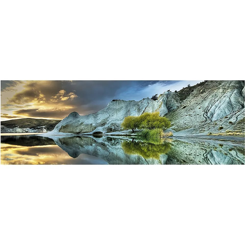 Panoramablick auf einen ruhigen See, der weiße Felsen, grüne Bäume und einen bewölkten Sonnenuntergangspass spiegelt.