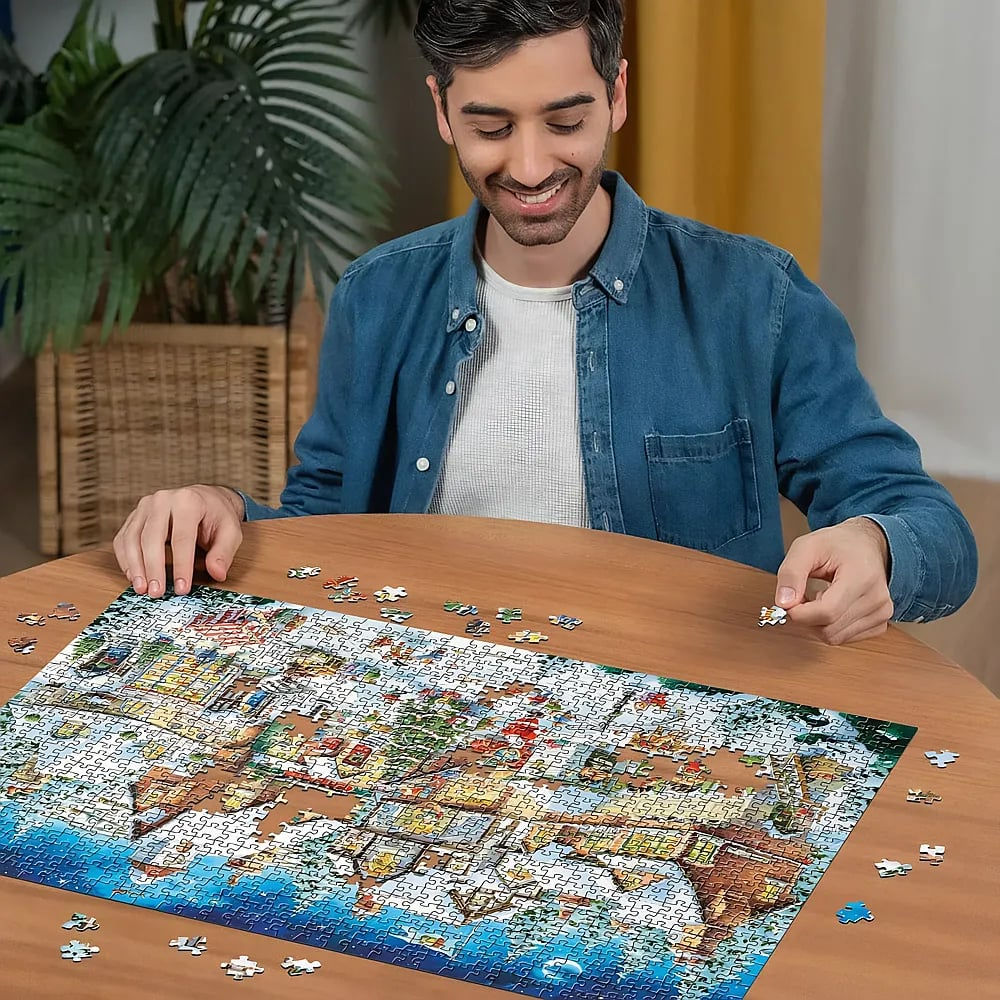 Un uomo sorridente siede a un tavolo di legno componendo un grande puzzle.