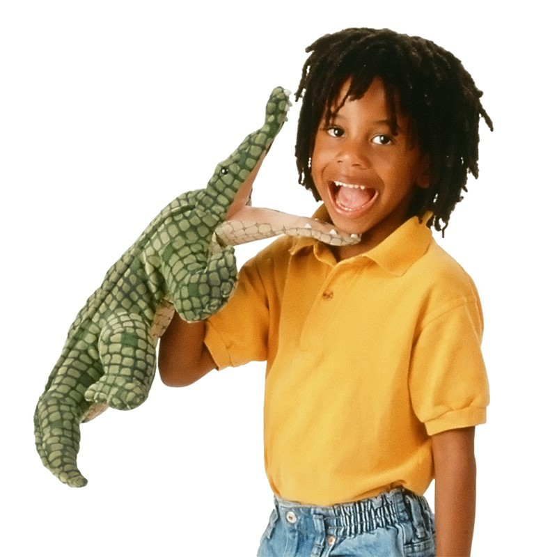 Un jeune enfant avec des dreadlocks portant une chemise jaune tient une marionnette de crocodile.