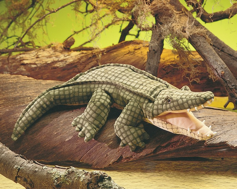 Un crocodile en peluche à la bouche ouverte repose sur une grande bûche devant un fond vert flou.