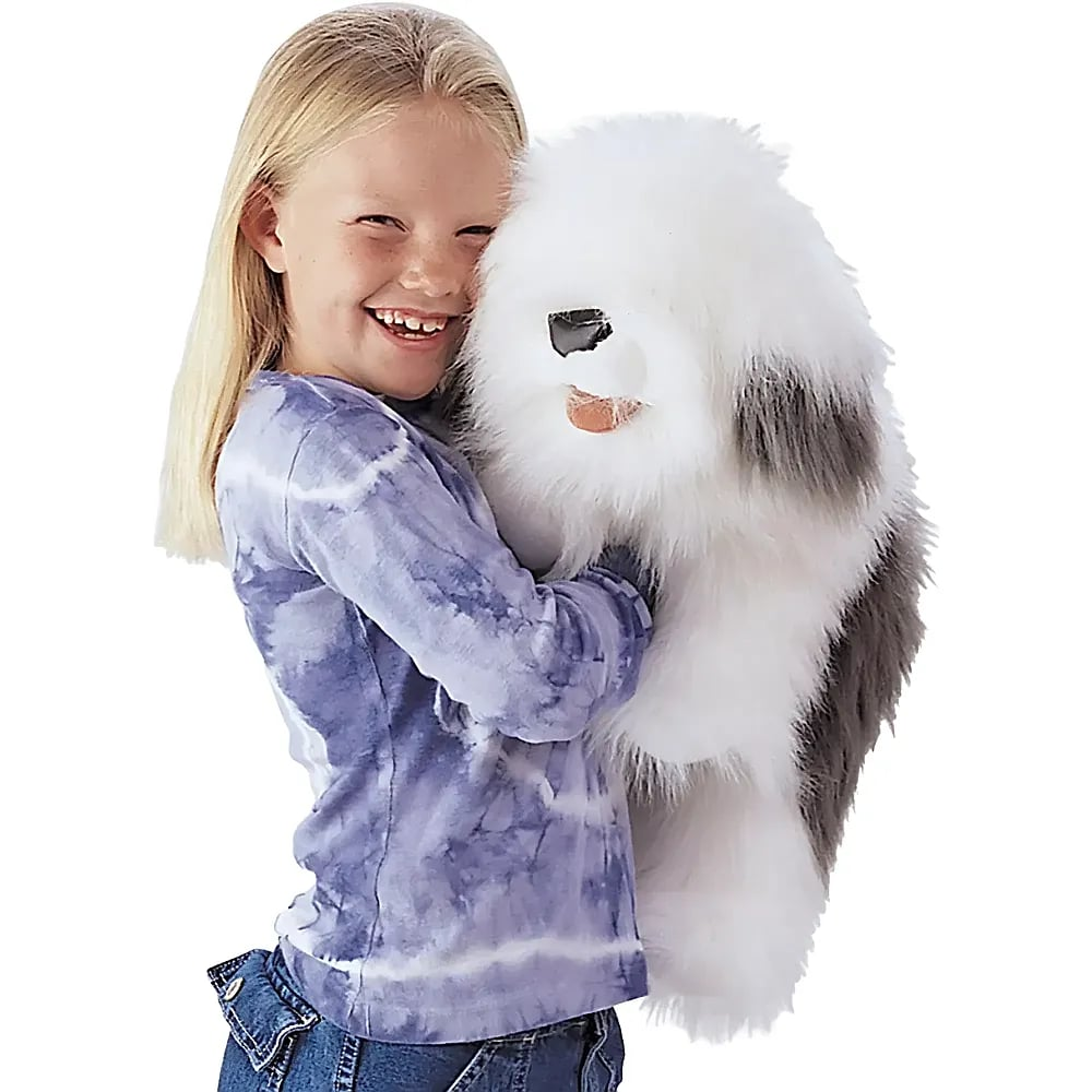 Une fillette blonde souriante en t-shirt tie-dye serre dans ses bras un grand chien en peluche sur fond blanc.