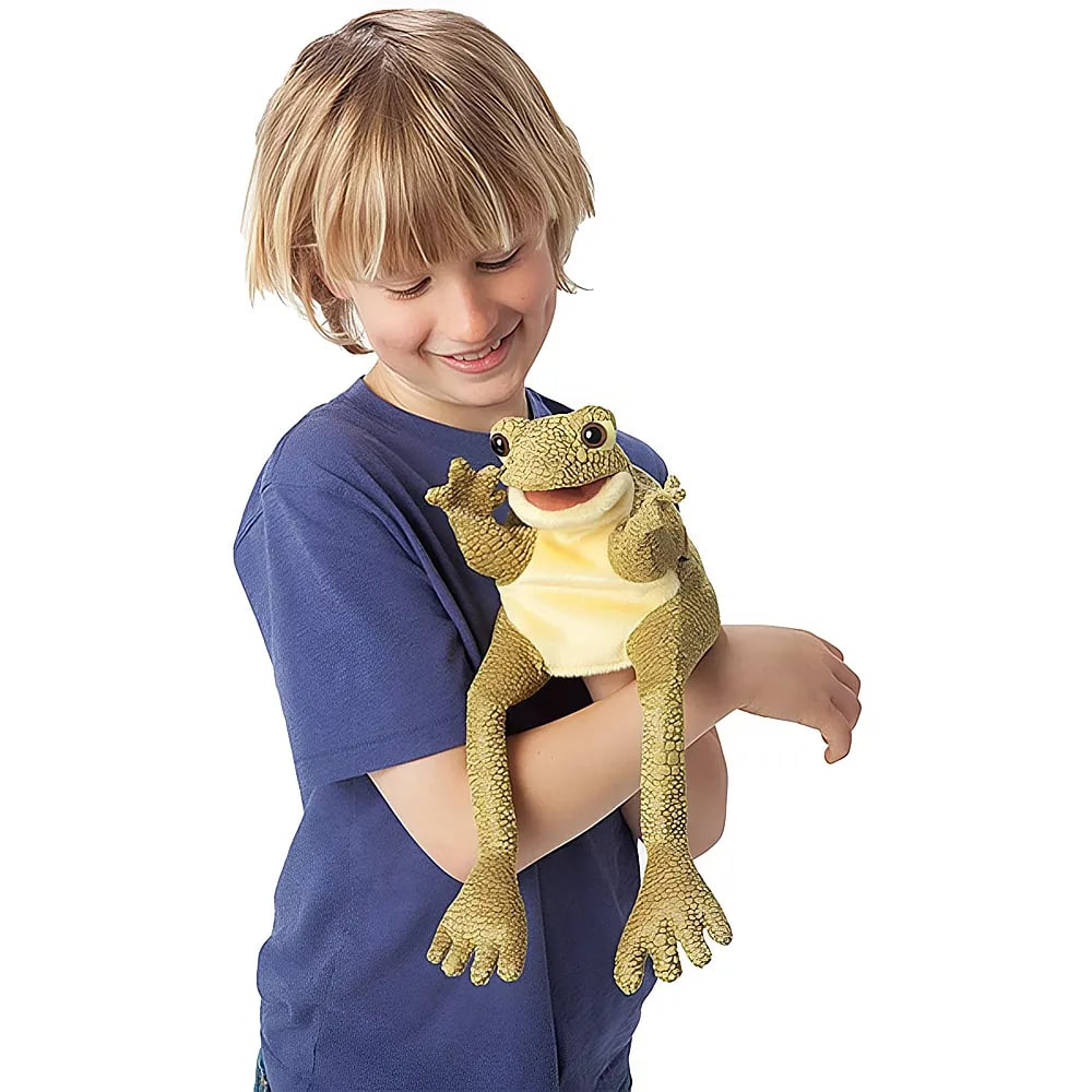 Ein blondes Kind in einem blauen T-Shirt lächelt und hält eine grüne Frosch-Handpuppe an seinem Arm.