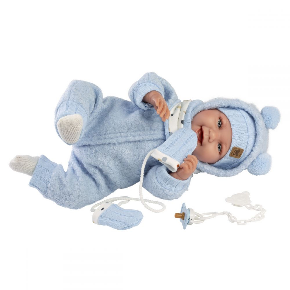 Una bambola realistica con vestiti di peluche blu giace sulla schiena tenendo un ciuccio con cinturino.