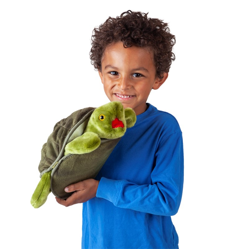 Ein junger Junge mit braunen, lockigen Haaren und einem blauen Pullover hält eine Plüschschildkröte.