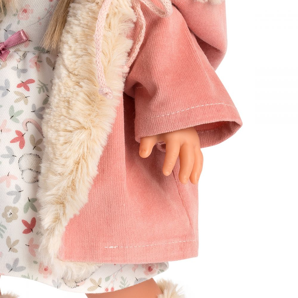 Eine Puppe mit einem rosa Mantel mit Fellbesatz über einem geblümten Kleid.