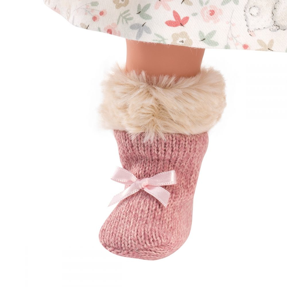 Eine rosa Strickstiefelletten mit Fellkragen und Schleife an einem Puppenbein unter einem gemusterten Rock.