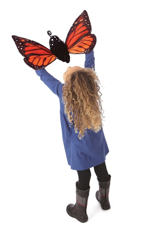Une fille blonde en robe bleue soulève une grande peluche papillon monarque.