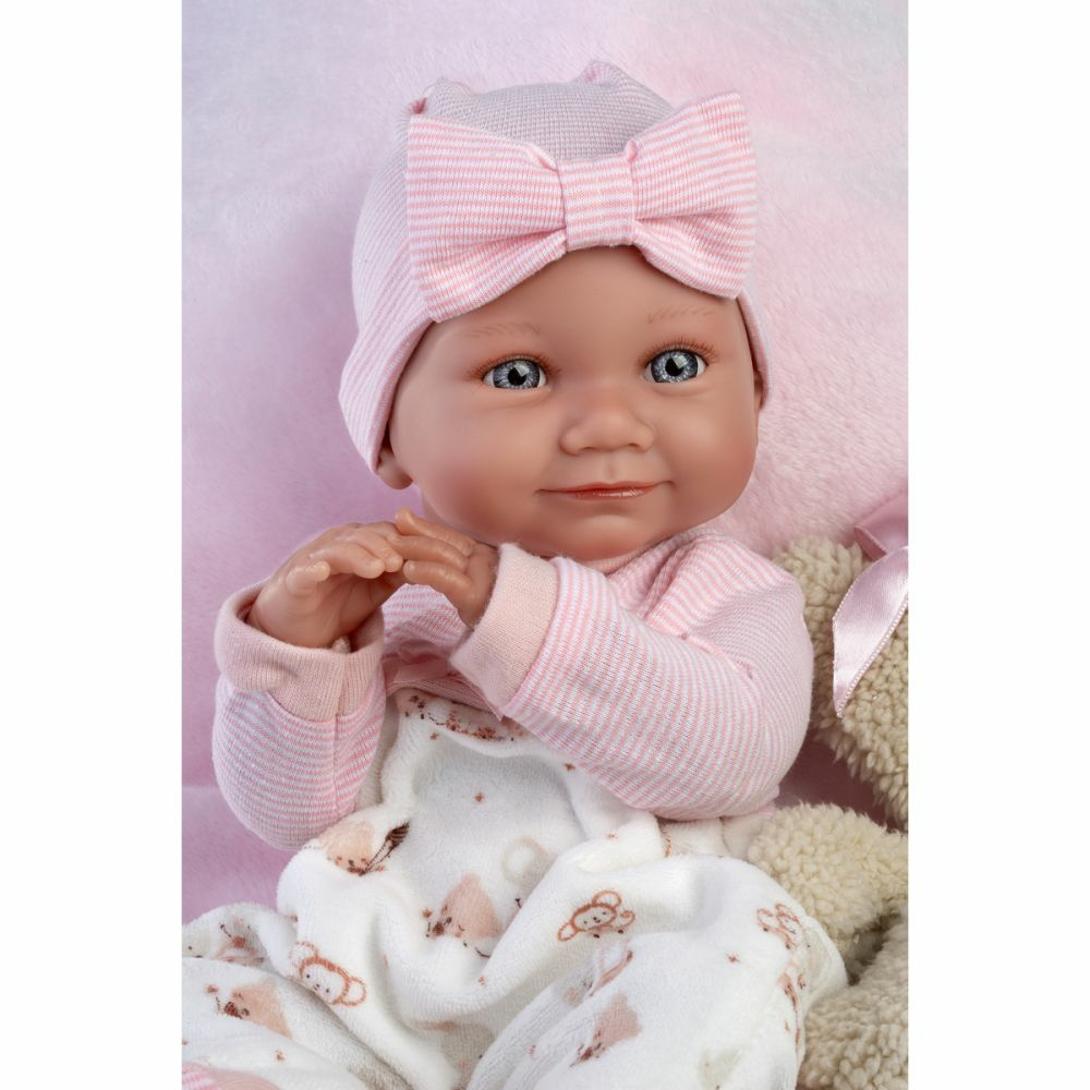 Una bambola realistica con cappello rosa, maglia a righe e coperta con motivi su sfondo rosa.