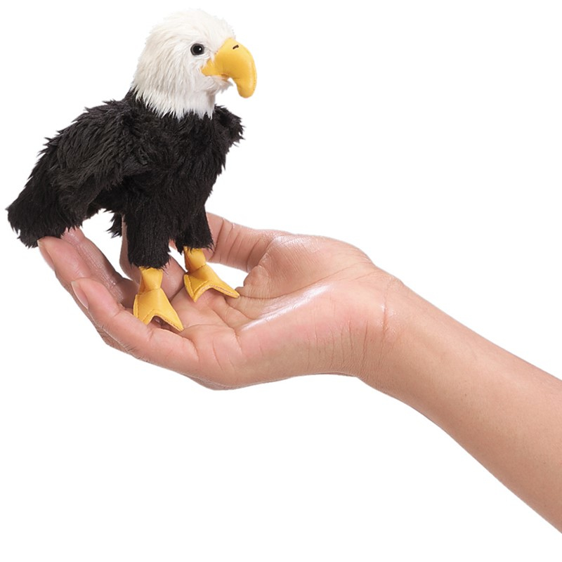 Une main ouverte tient une petite peluche d'aigle avec une tête blanche, un corps noir et un bec jaune.