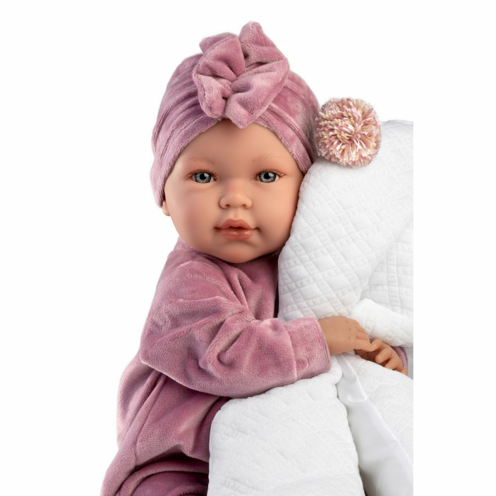 Un poupon réaliste en habit rose et turban tient une couverture blanche.