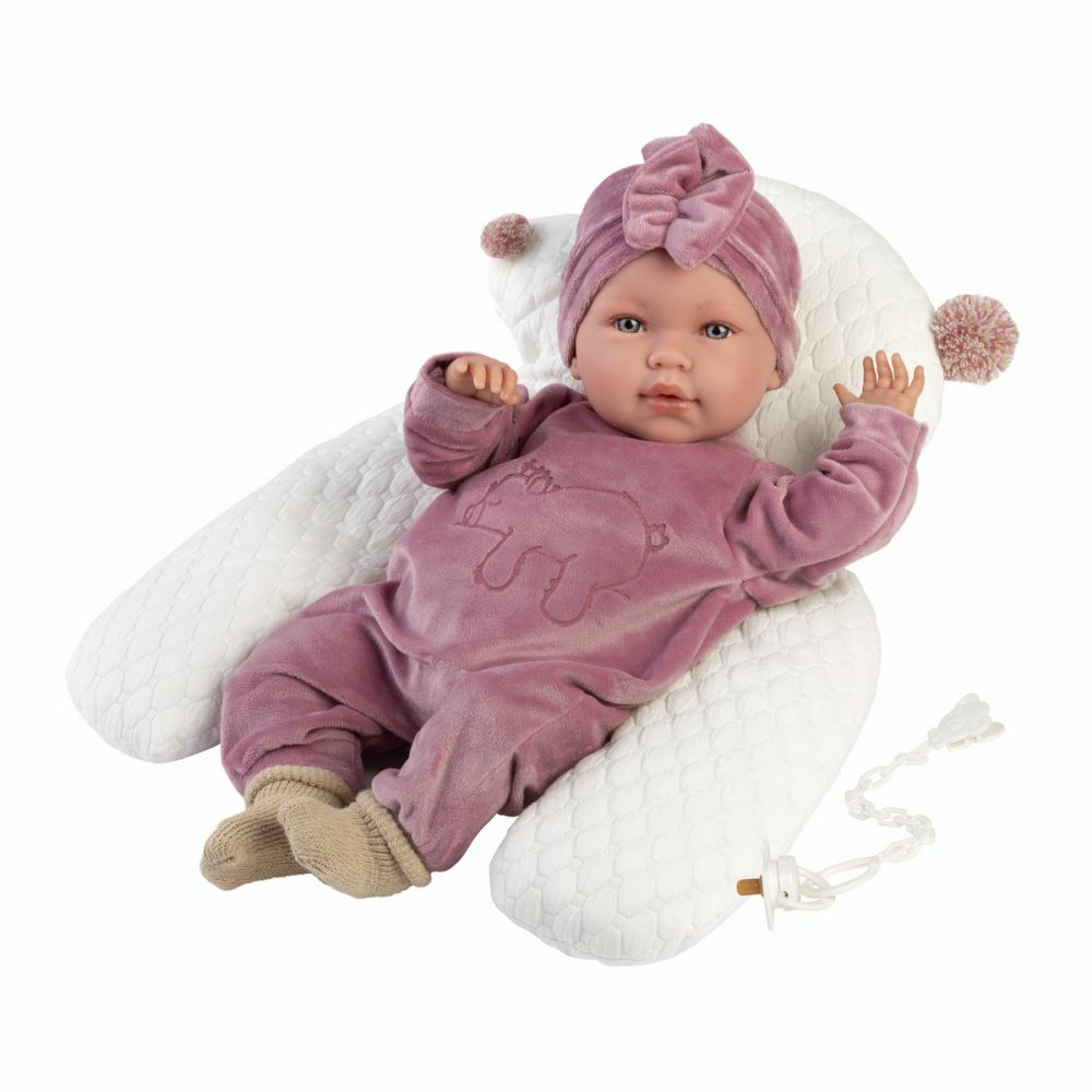 Un poupon en grenouillère et bonnet roses est allongé sur un coussin blanc avec une tétine.
