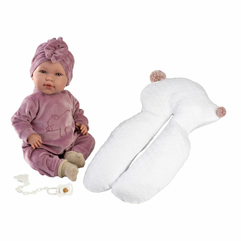 Un poupon en vêtements roses avec un bonnet, à côté d'un coussin d'allaitement blanc et d'une tétine avec chaîne.