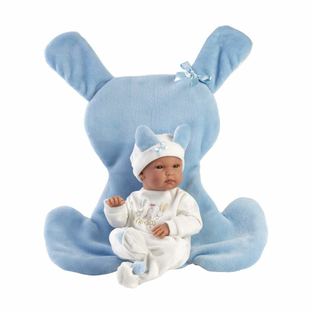 Una bambola realistica in tutina da coniglietto bianco siede davanti a un grande cuscino blu.