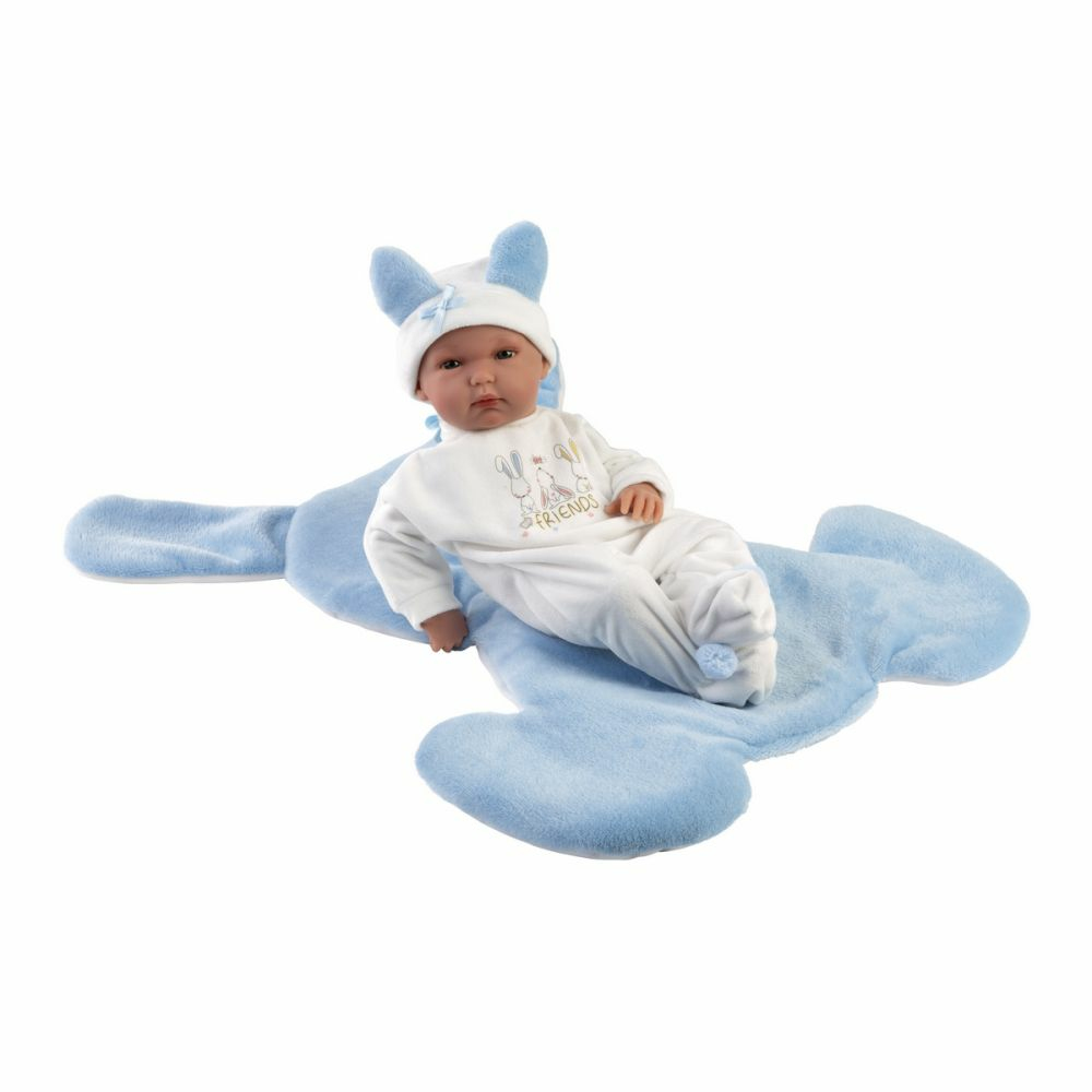 Una bambola con abiti bianchi e blu giace su una coperta morbida e celeste.