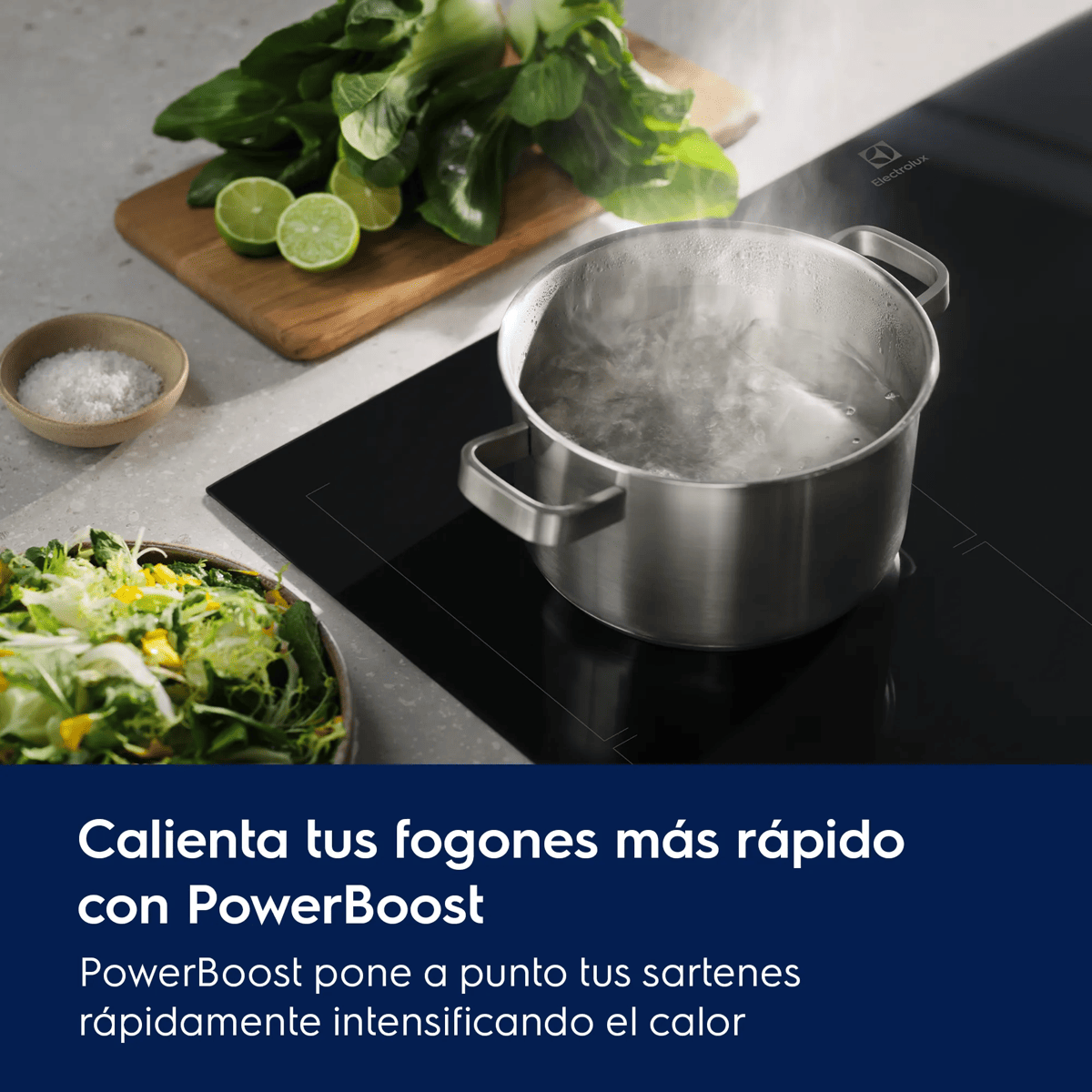 Una olla hirviendo en una placa de inducción, con ensalada, limas y verduras de hoja en una tabla de madera.