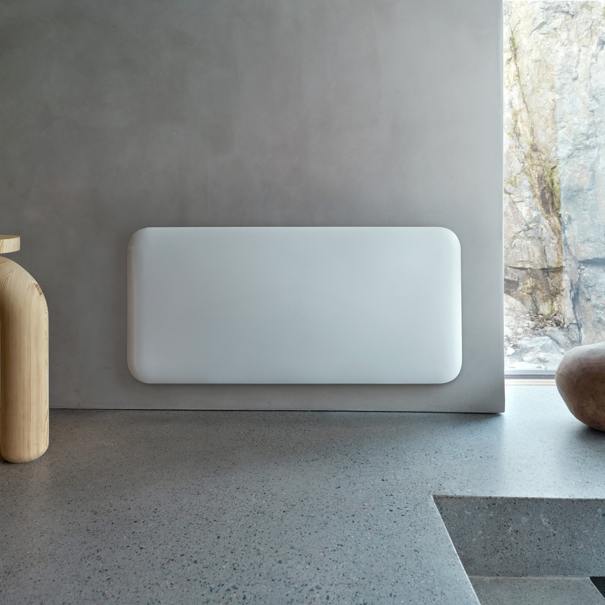 Un termosifone rettangolare bianco su parete grigia, con decoro in legno e vista rocciosa sullo sfondo.