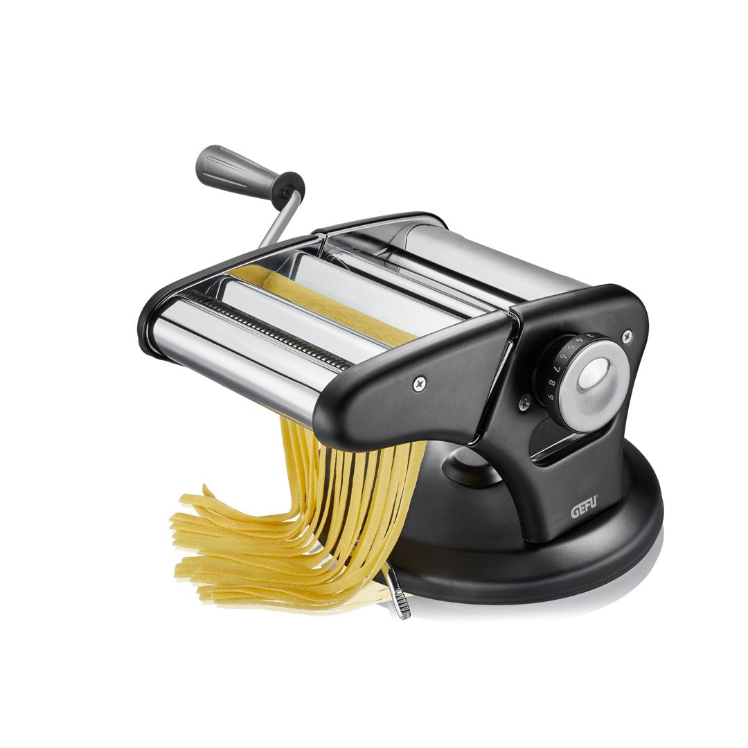 Una macchina per pasta in acciaio inossidabile con base e manico neri, che estrude tagliatelle gialle su sfondo bianco.