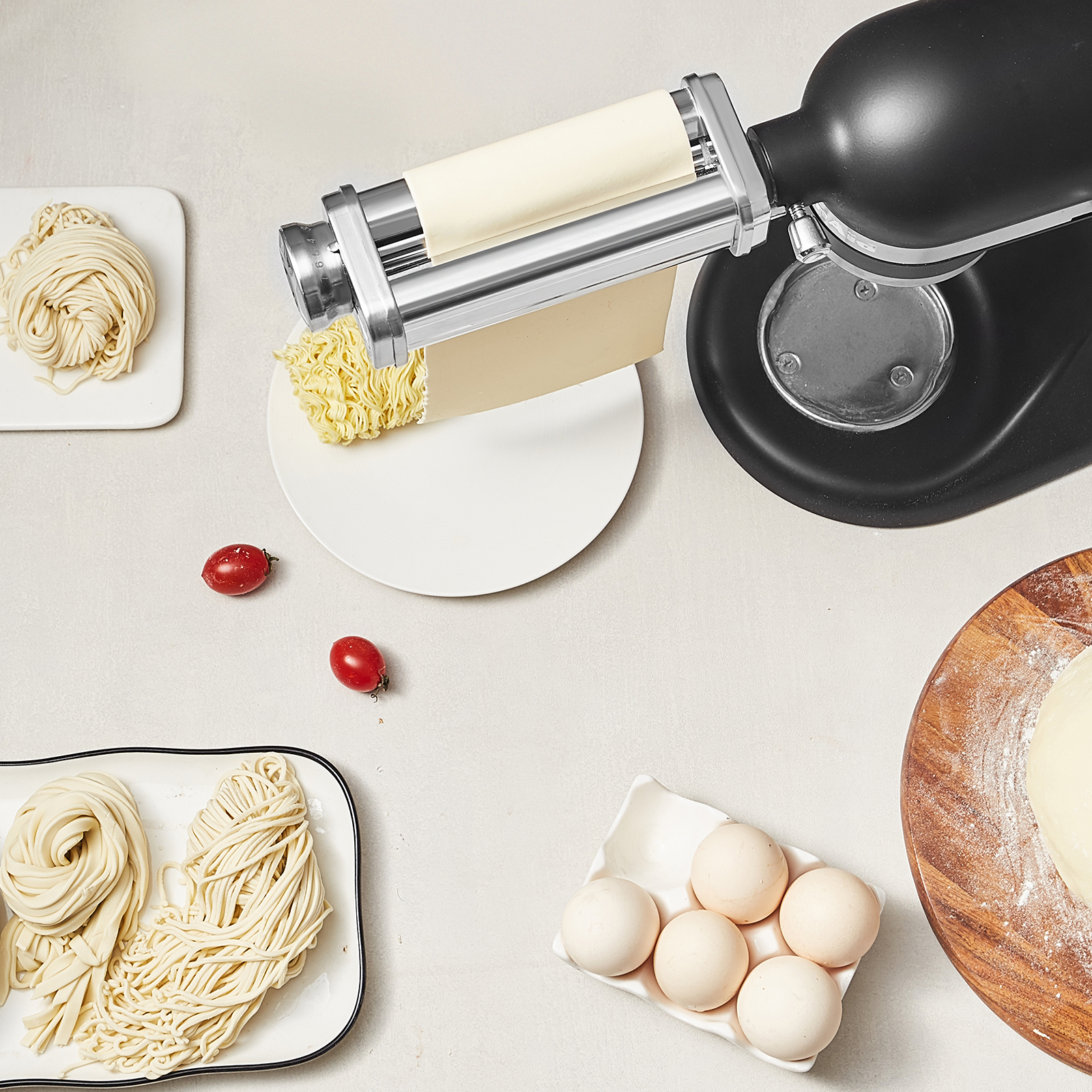 Batidora negra con accesorio para pasta, fideos frescos, huevos, tomates y masa en tabla.