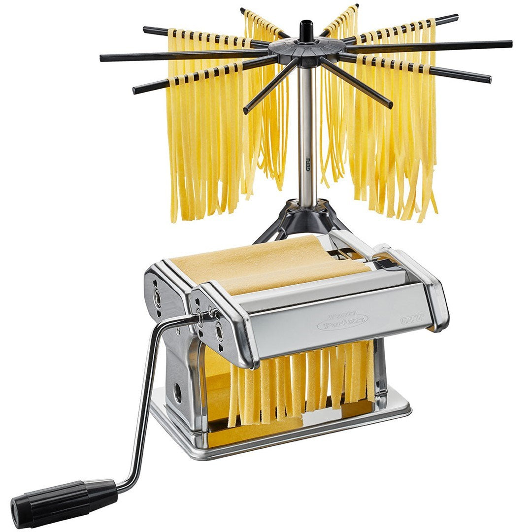 Una macchina per la pasta in acciaio inox con manovella e uno stendipasta circolare con tagliatelle fresche.