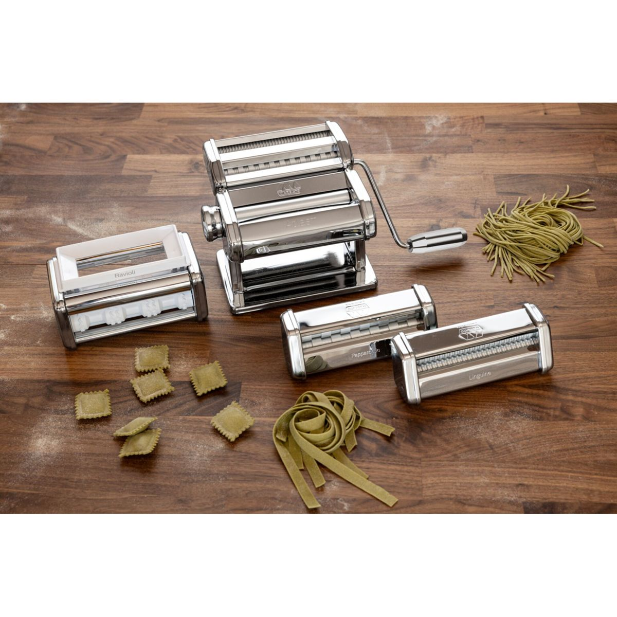 Macchina per pasta in acciaio inox con accessori e pasta verde su tavolo in legno.