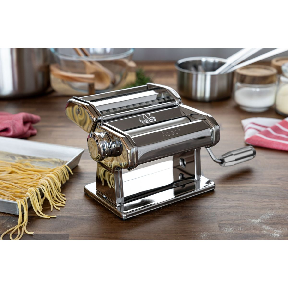 Una macchina per pasta in cromo su un bancone di legno con pasta fresca su un vassoio.