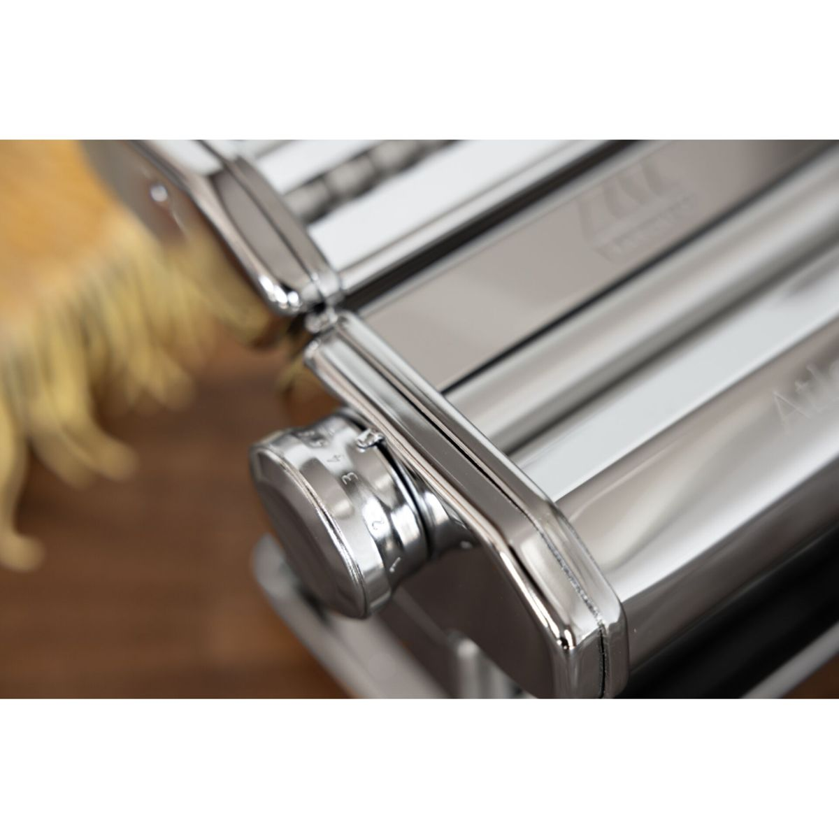 Primo piano di una macchina per pasta in cromo lucido con manopola di regolazione dello spessore su legno.