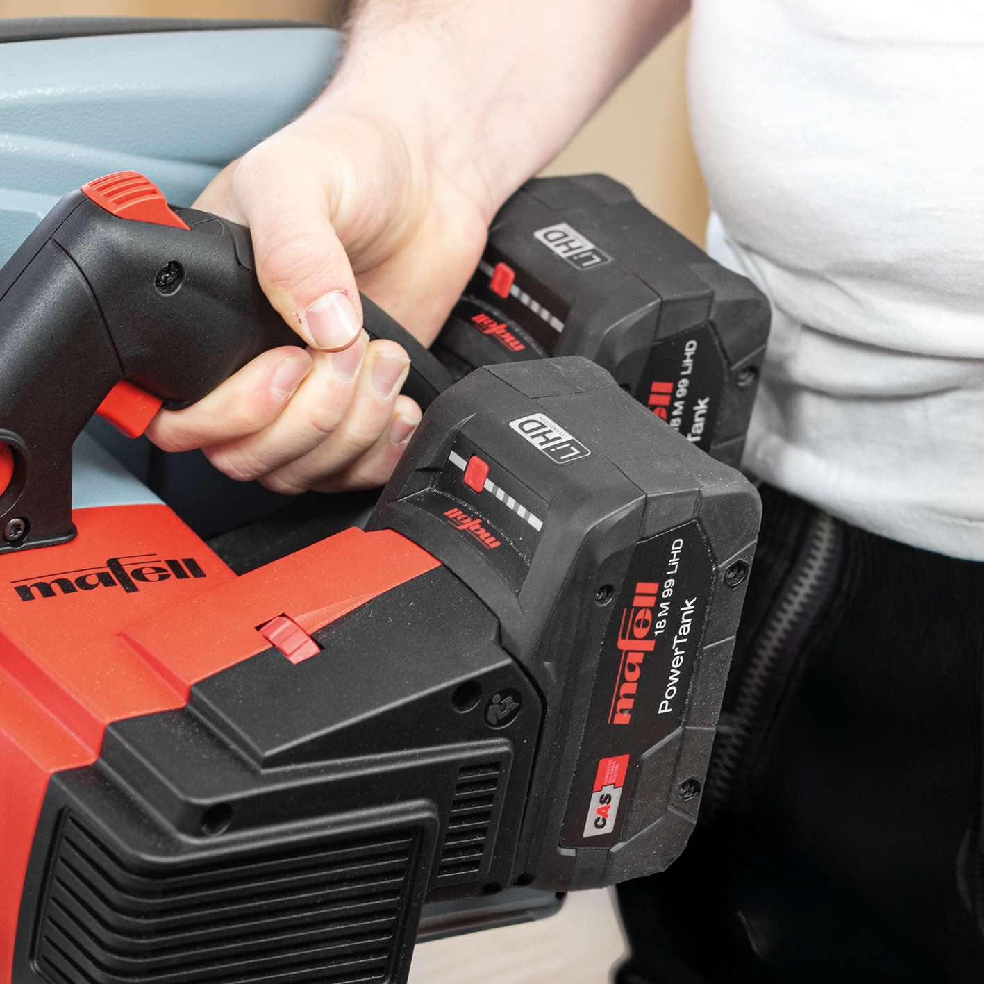 Eine Person hält eine rot-schwarze Mafell-Akkubaumaschine mit zwei großen Batterien.