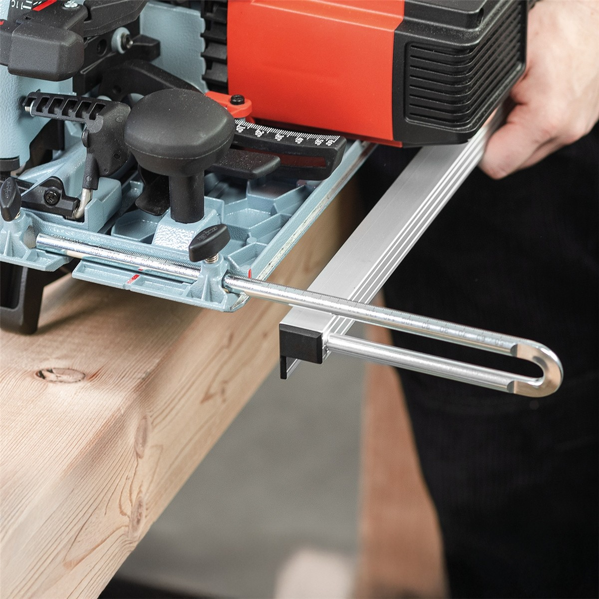 Nahaufnahme eines blau-roten Elektrowerkzeugs mit Aluminium-Führungsschiene auf einem Holzbalken.