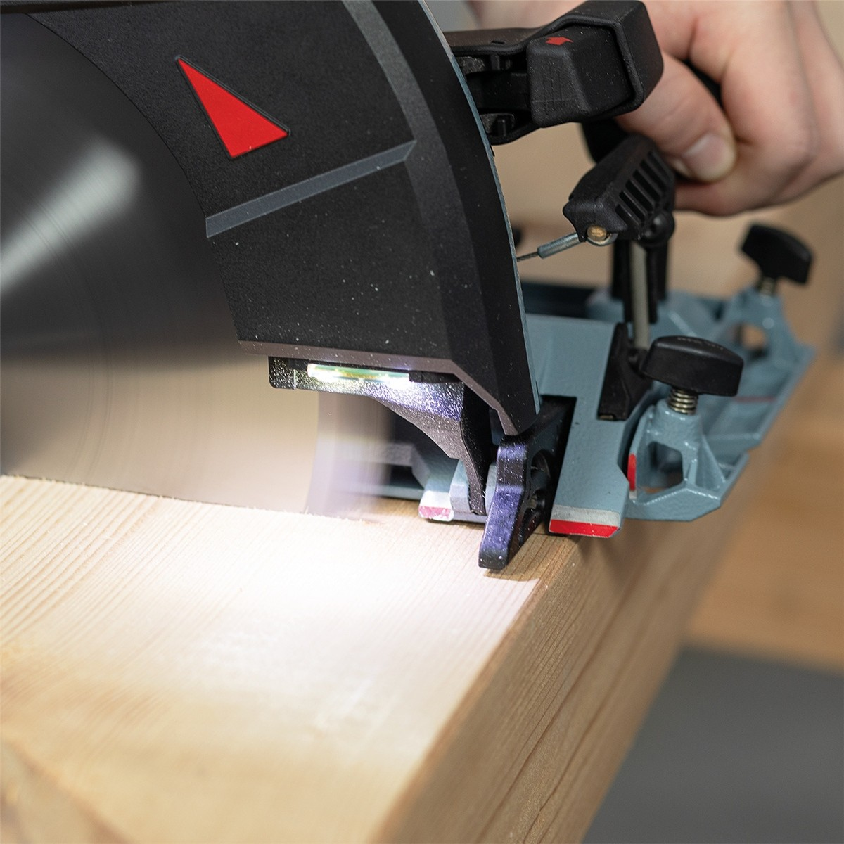 Eine Hand führt eine Kreissäge, die mit einer LED-Leuchte ausgestattet ist, beim Schnitt durch einen Holzbalken.