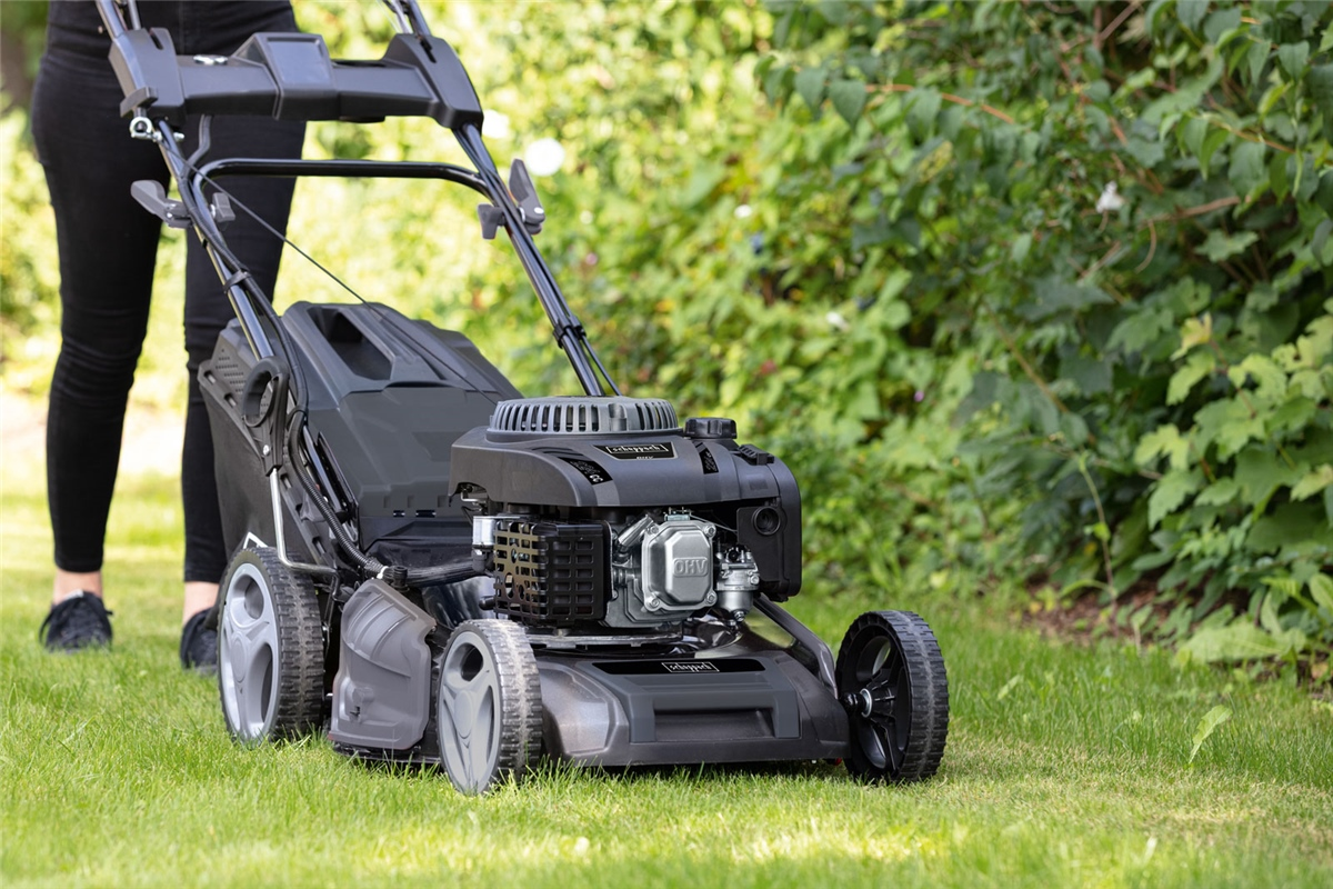 Eine Person mäht den Rasen mit einem modernen schwarzen Rasenmäher im Garten.