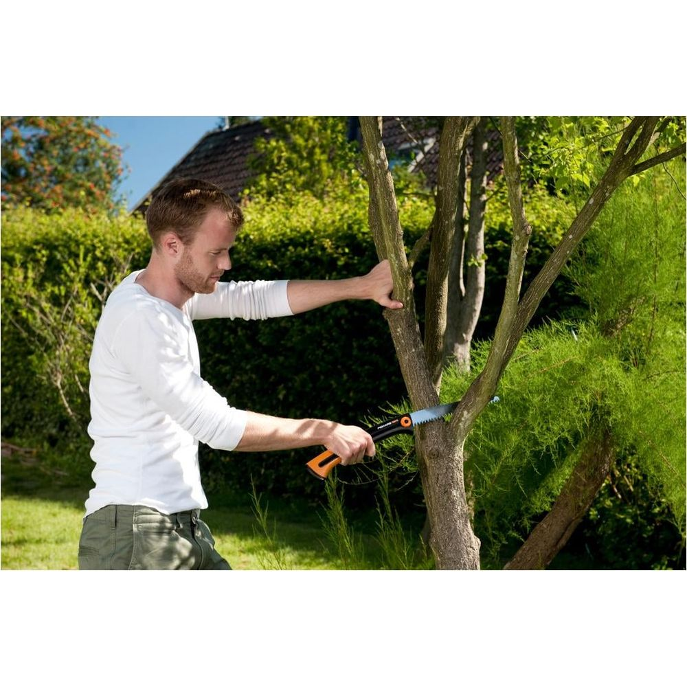 Ein Mann in weißem Shirt schneidet im Garten mit einer Handsäge einen Ast.