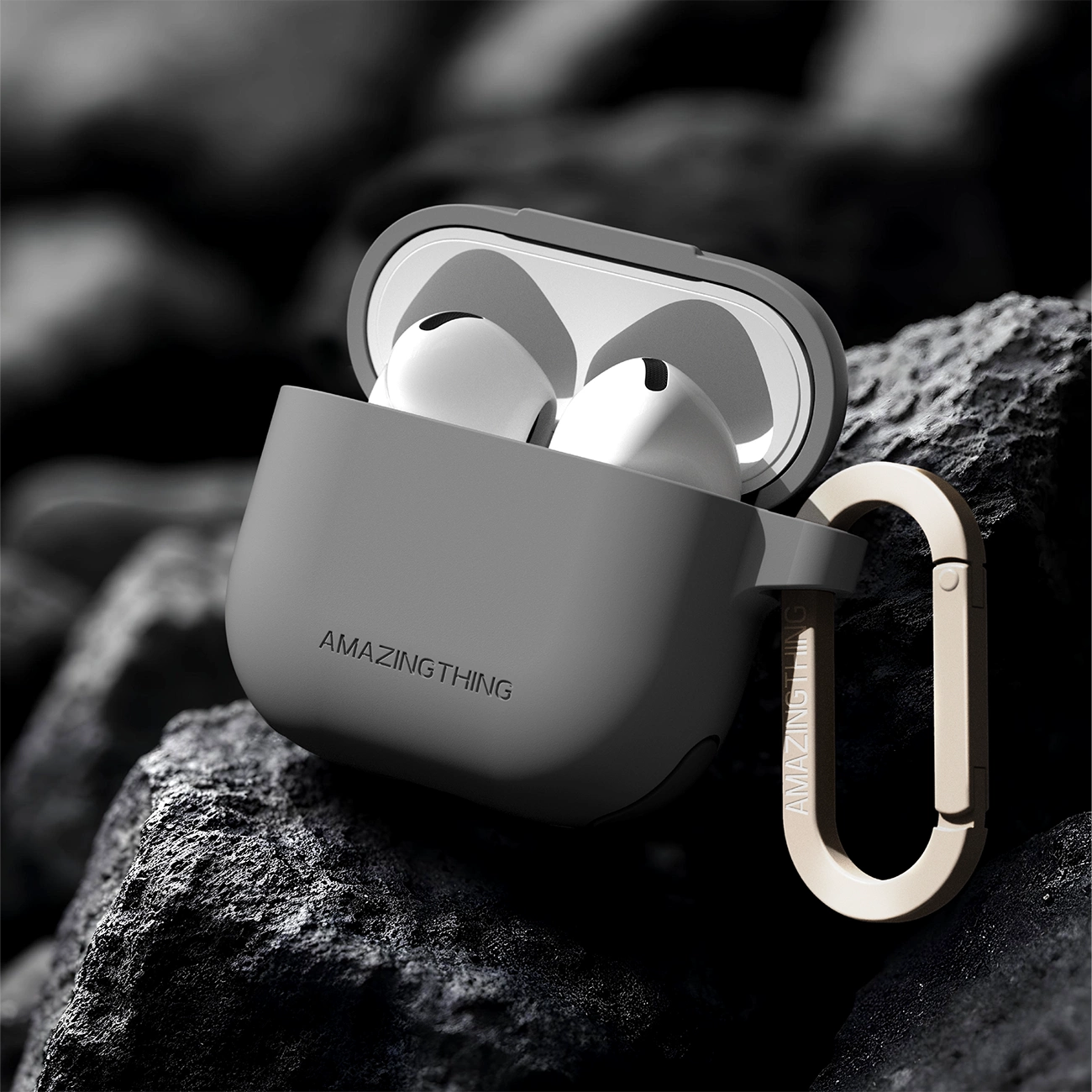 Custodia grigia per AirPods Pro con moschettone, posizionata su rocce scure.