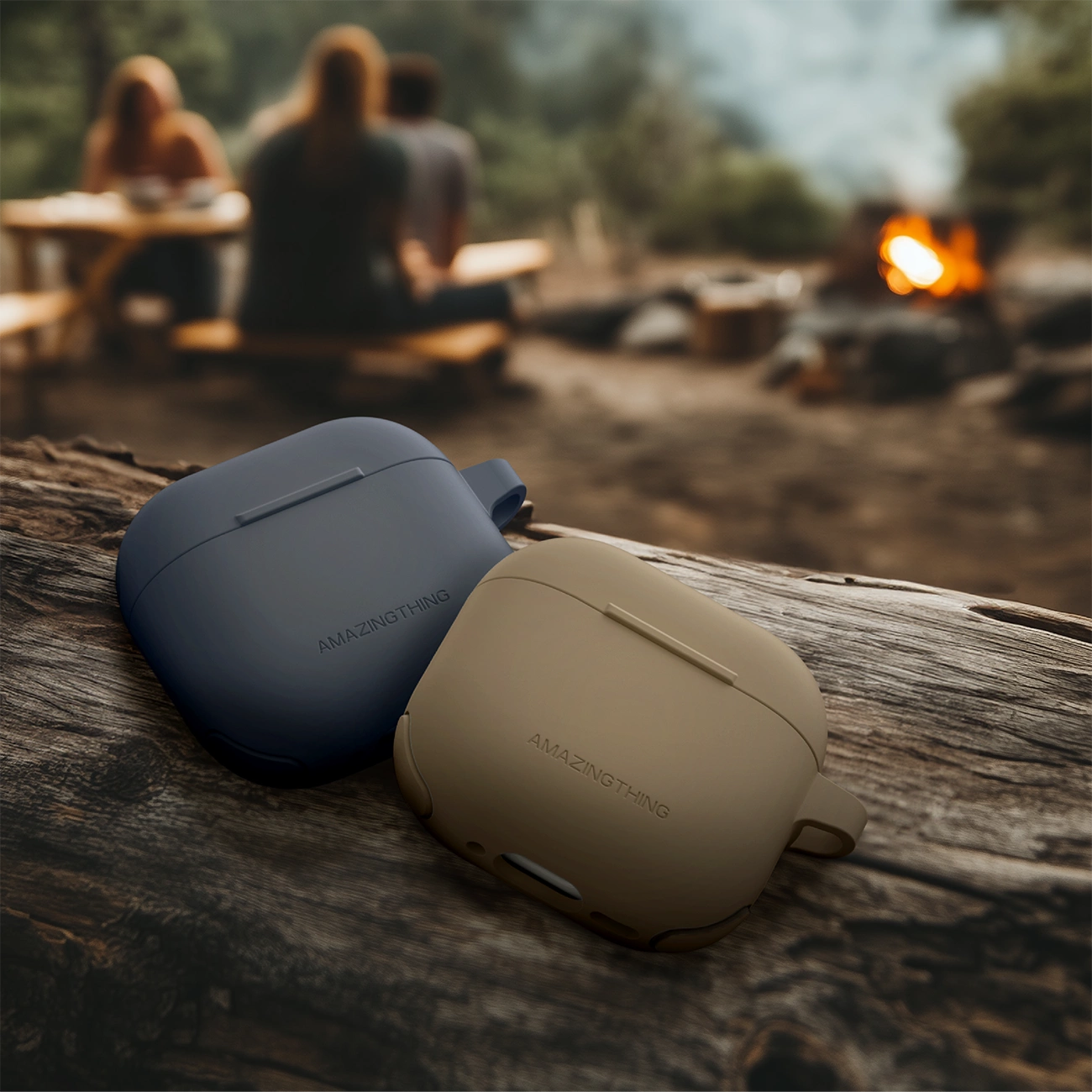 Due custodie per auricolari wireless blu e beige poggiano su un tronco davanti a un fuoco da campo sfocato.