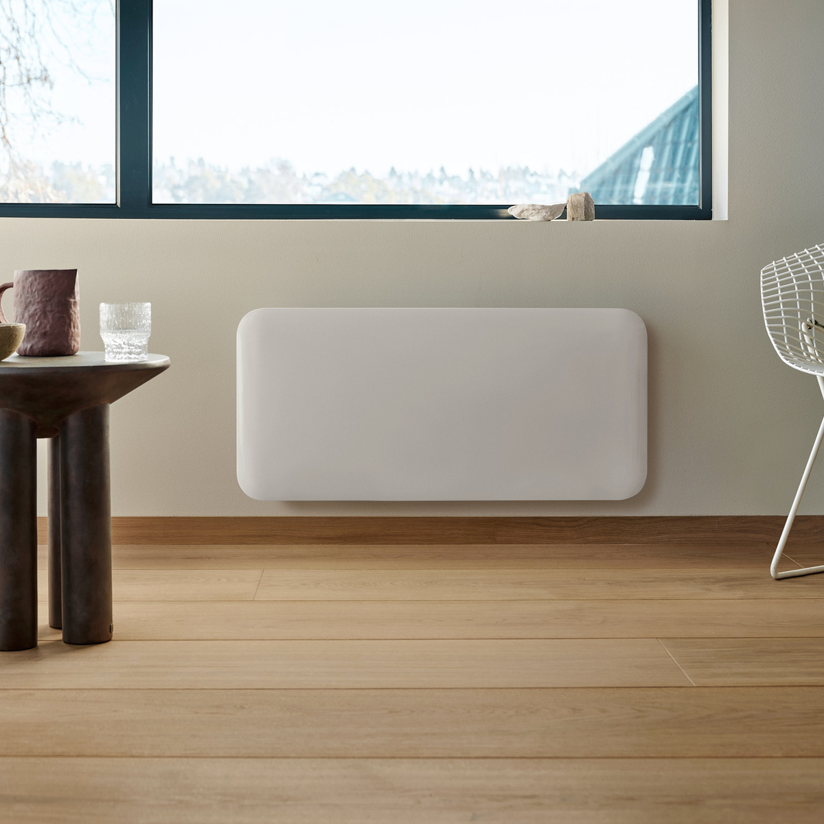 Un termosifone bianco a parete in una stanza luminosa con pavimento in legno e grande finestra.